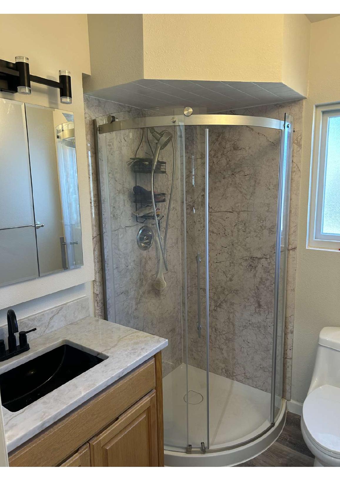 Bathroom renovation with curved glass shower and marble-patterned walls